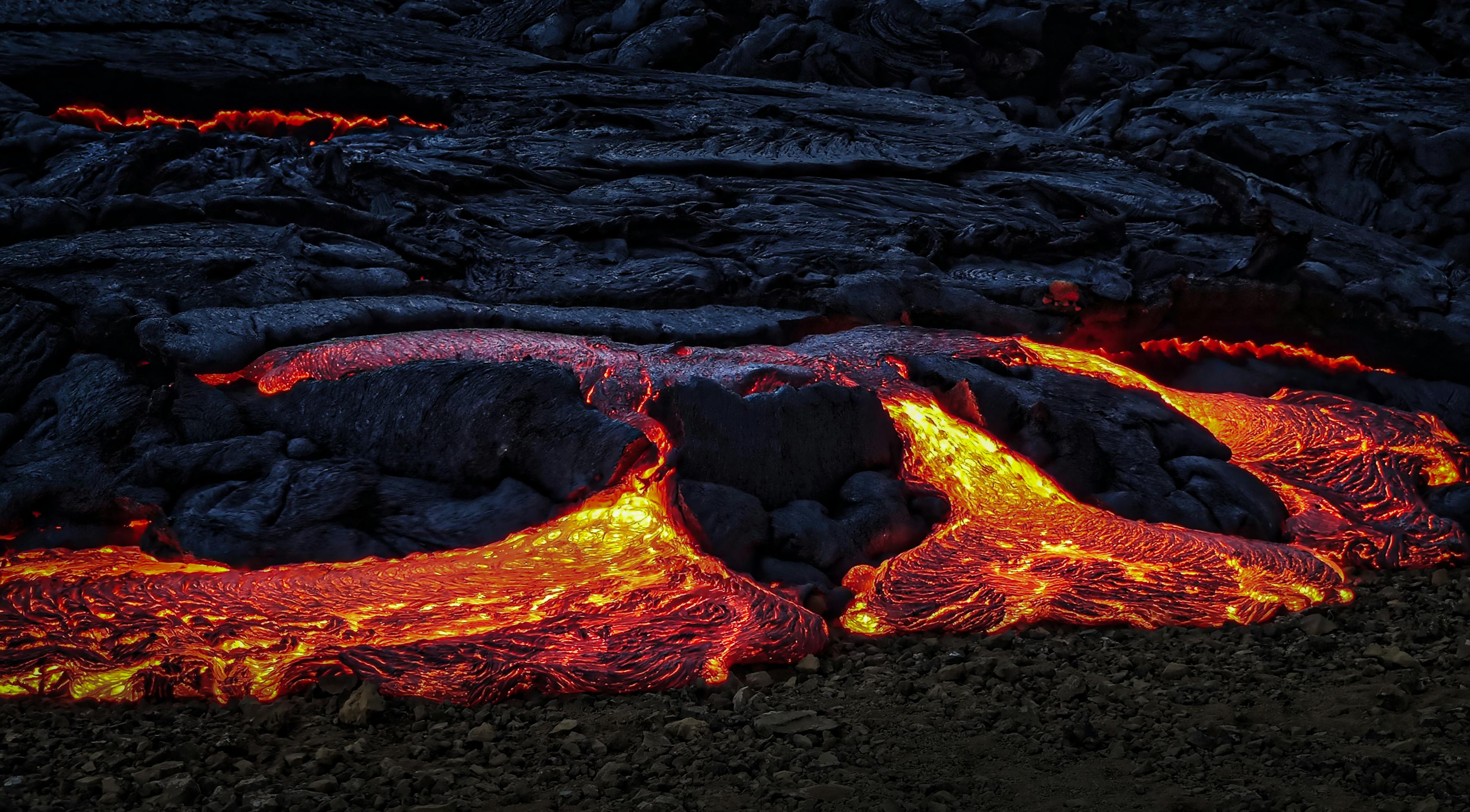 Captivating image of vibrant molten lava flowing over dark rocks during twilight.