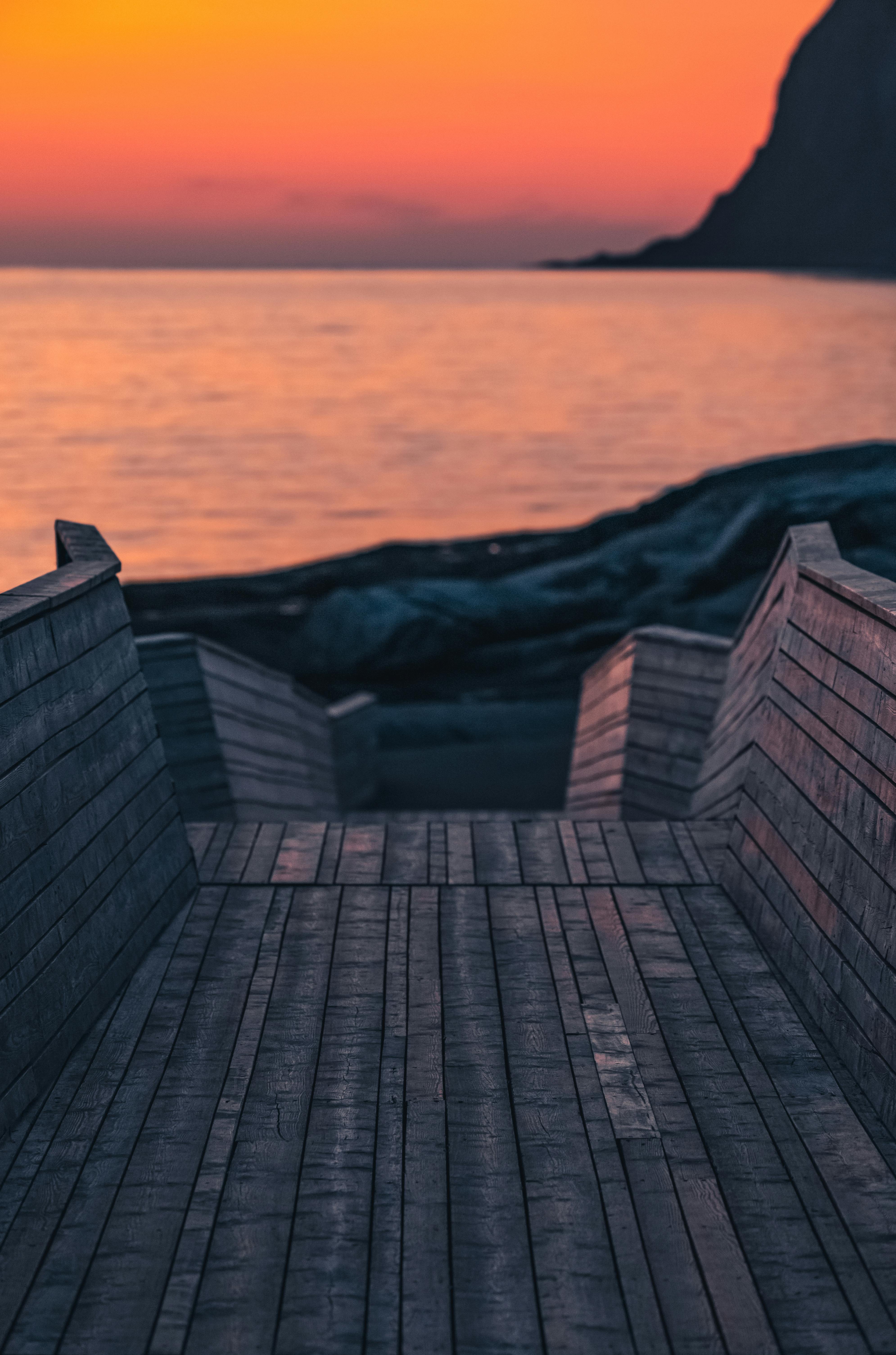 Wooden stair placed near calm rippled sea water running against coast under sunset sky in summer time
