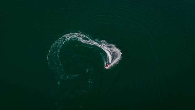 Dynamic aerial photo of a jet ski making waves on a vast body of water with a swirling pattern.