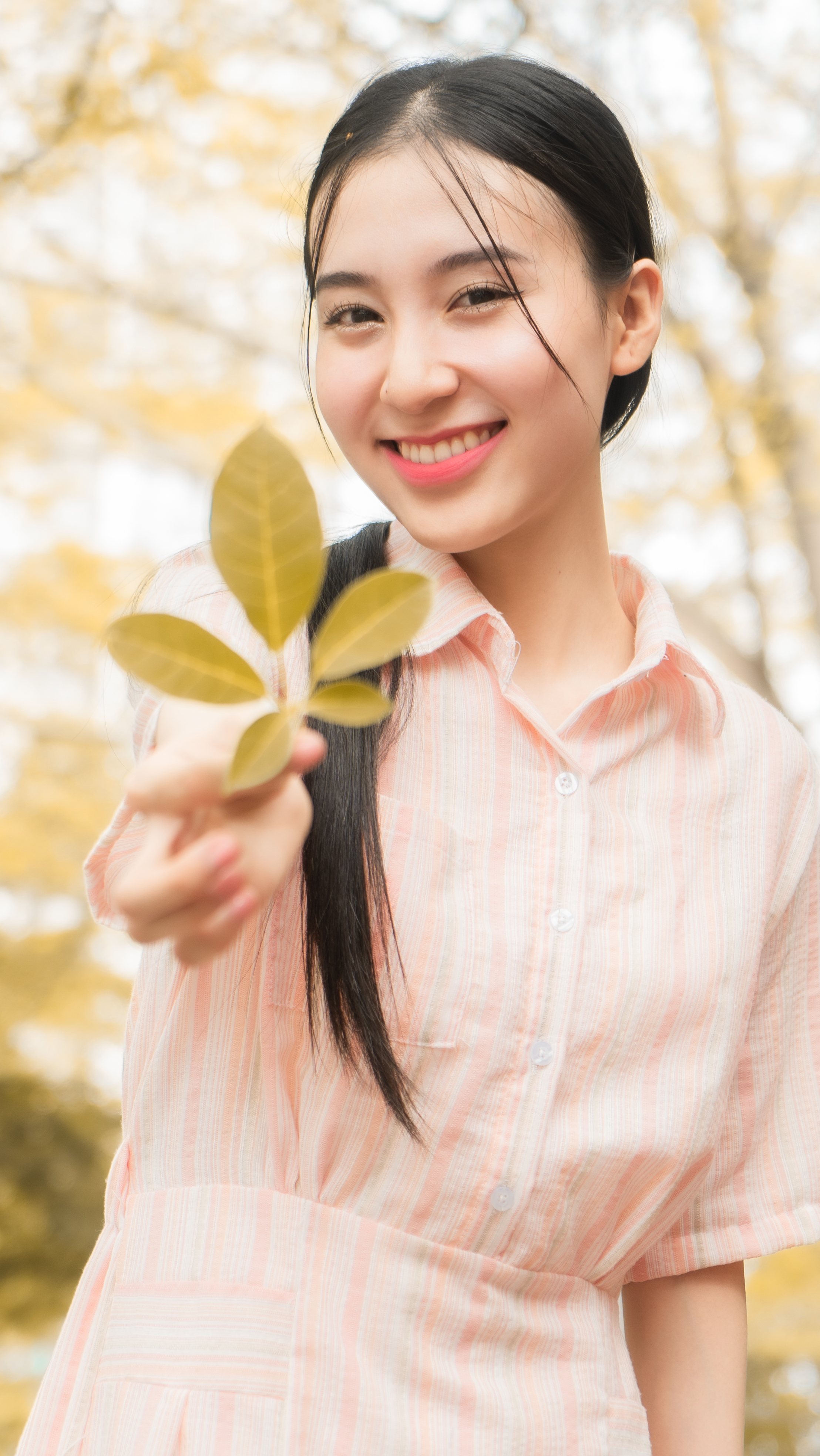Smiling woman enjoying a bright day, holding leaves in an outdoor setting.