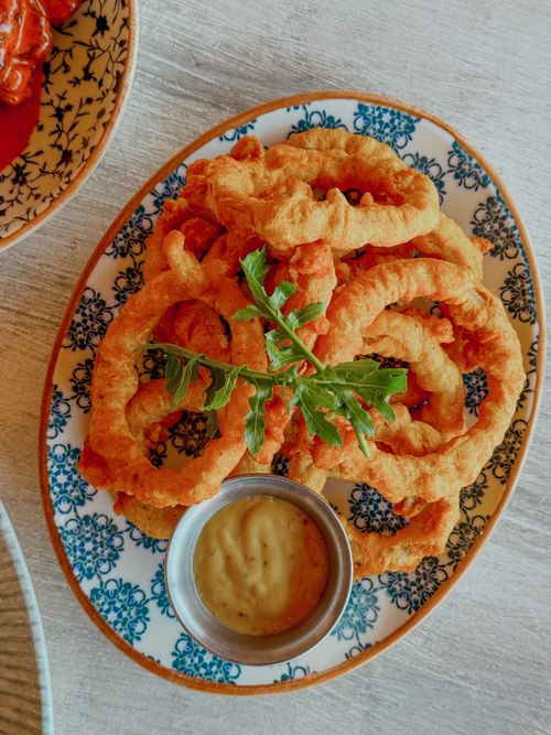 Free Golden fried calamari rings served with dipping sauce on an artistic floral plate. Stock Photo