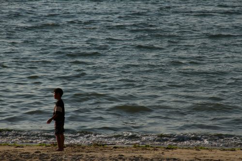 Free A young boy stands alone on a serene beach at dusk, facing the gentle waves. Stock Photo