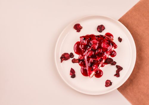 Free Aerial view of a raspberry-topped cheesecake slice with dried fruits on a plate. Stock Photo