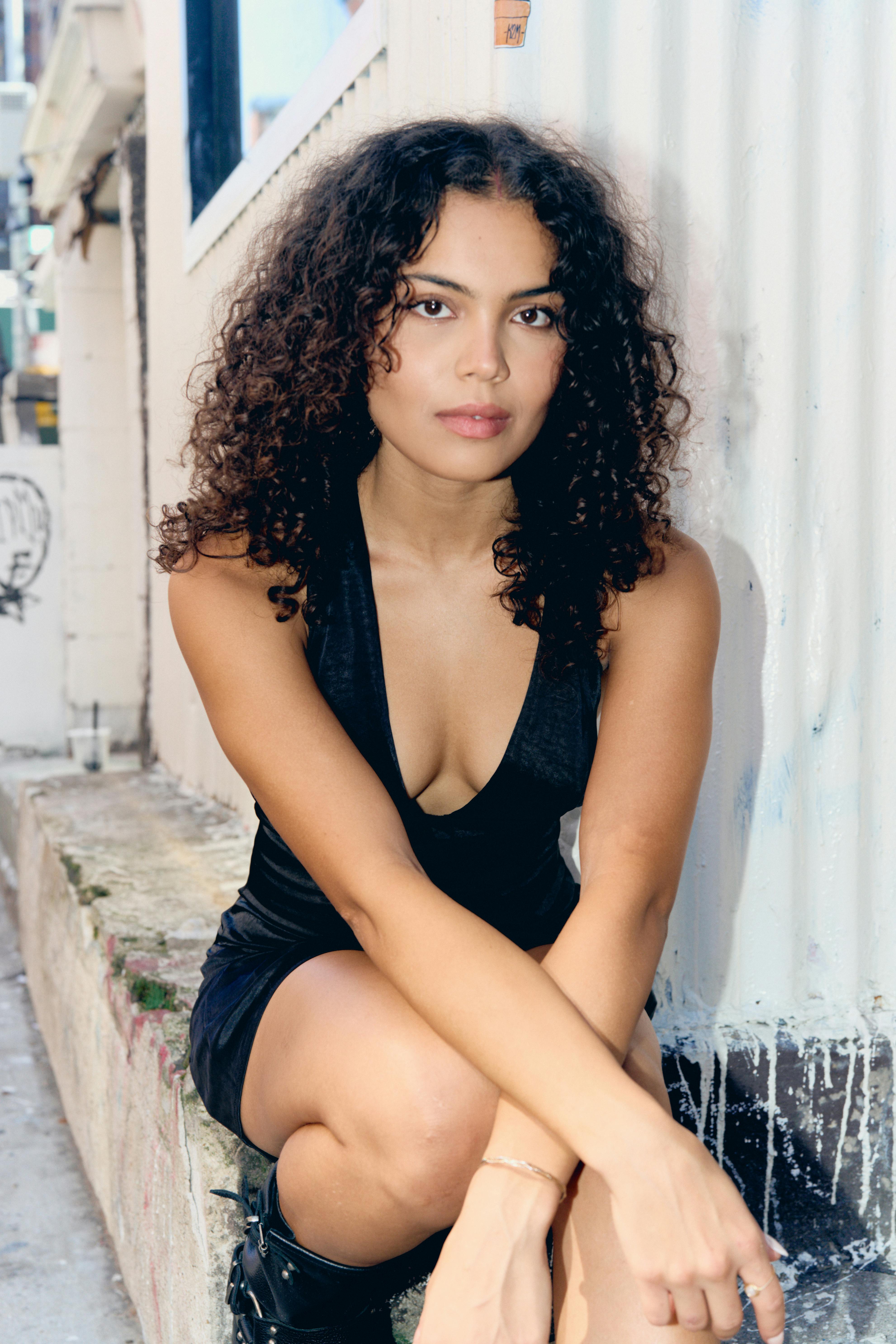 a woman with curly hair sitting on a wall