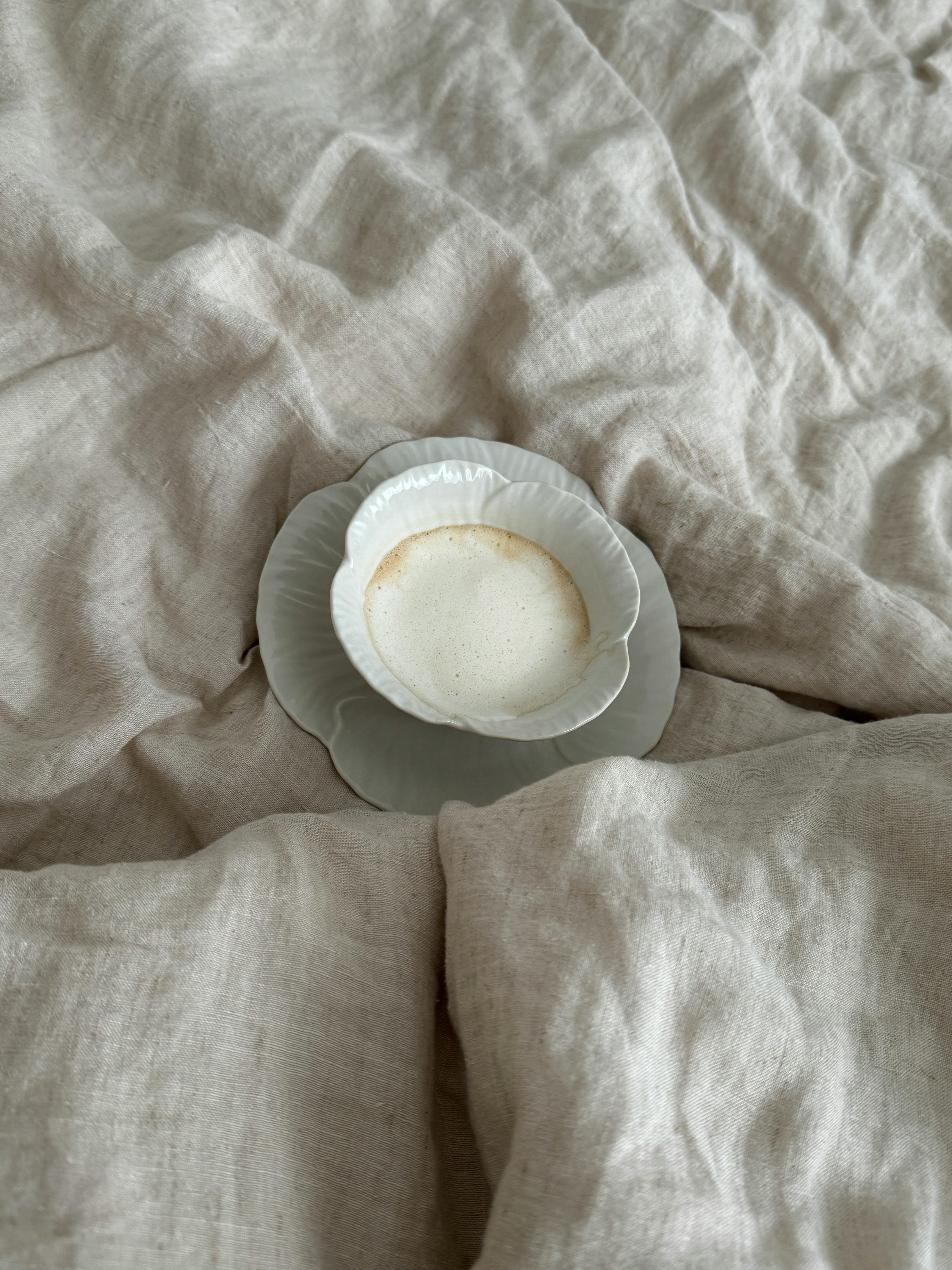 A serene scene of a cozy cup of coffee on soft linen bedding, exuding warmth and tranquility.