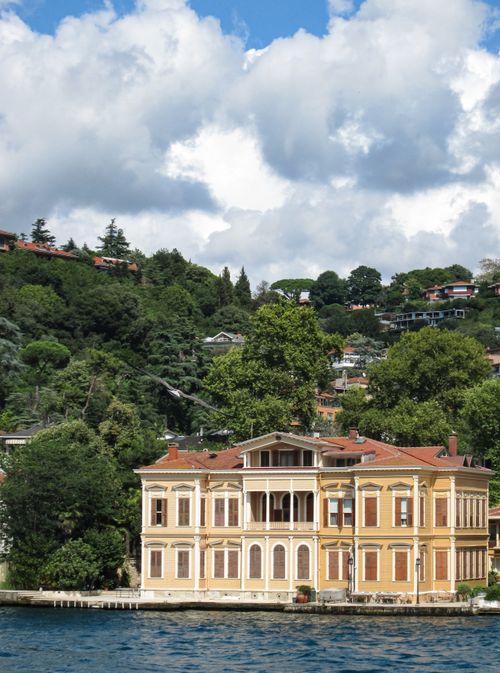 Free A picturesque villa by a serene water body, surrounded by lush greenery and a hilly backdrop. Stock Photo