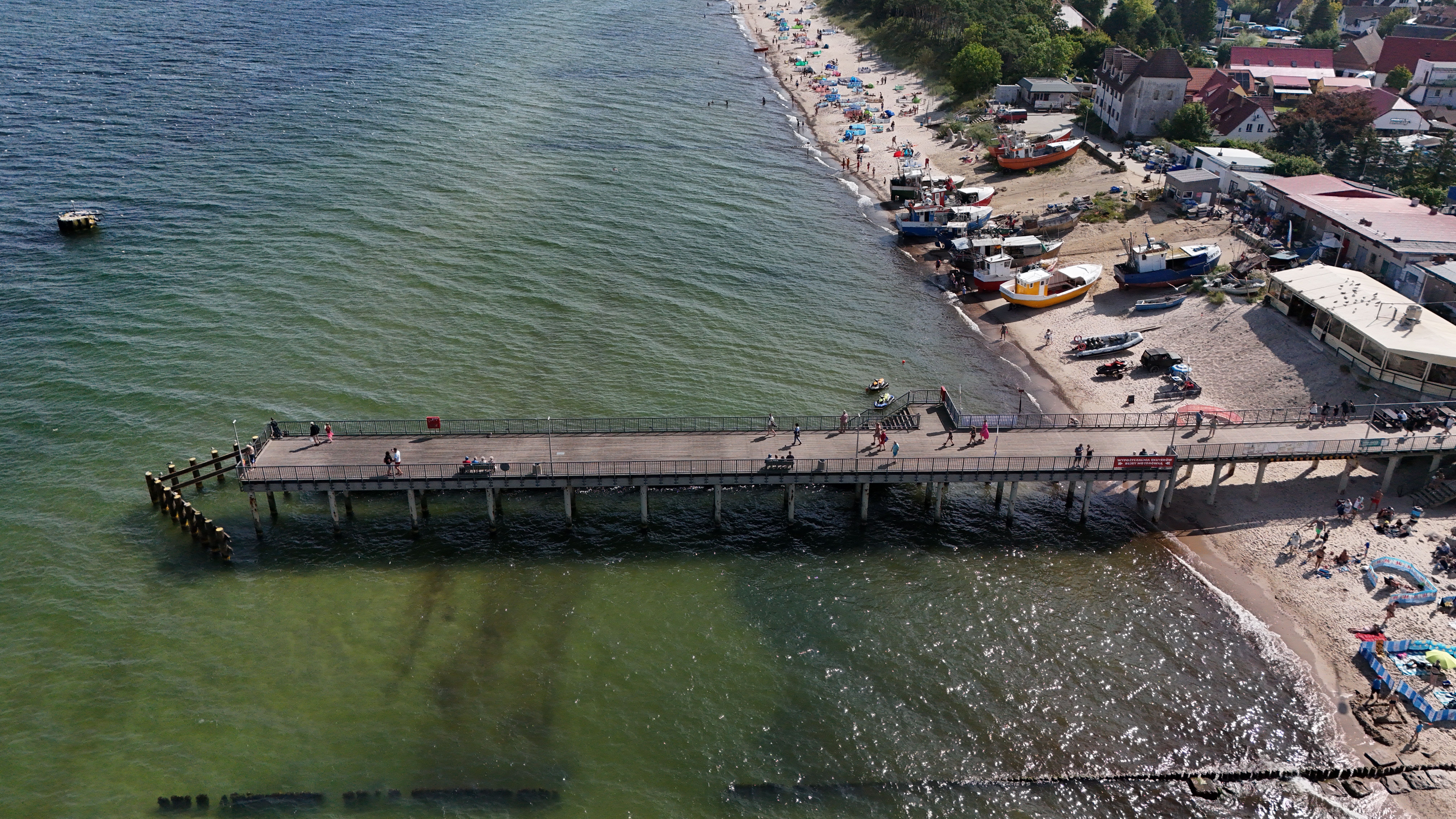 A scenic aerial view of a pier extending into the sea with a bustling beachfront. — Trójmiasto