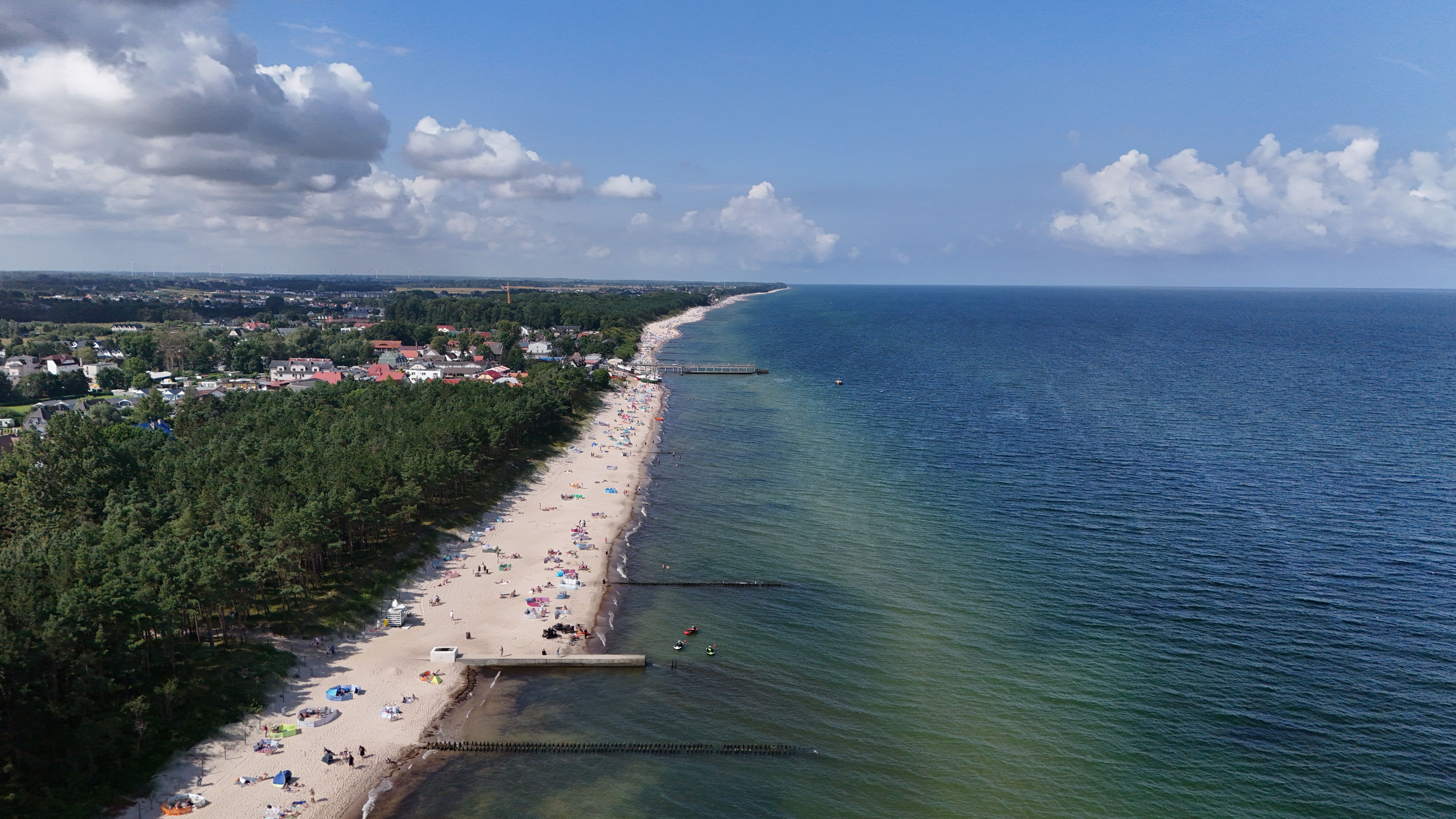 A breathtaking aerial shot of a sandy beach, vibrant ocean, and coastal town under a clear blue sky. — Trójmiasto