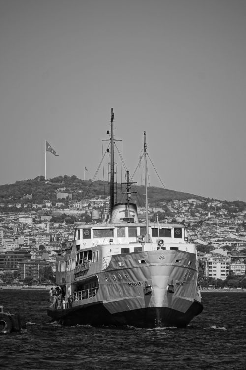 Free A classic ship approaches a harbor cityscape, captured in black and white for a timeless look. Stock Photo