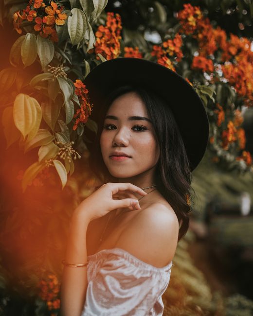 A stylish portrait of an elegant woman in a black hat surrounded by vibrant flowers during sunset.