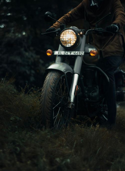Free Man on a vintage motorbike navigating a forest trail at dusk, showcasing adventure and exploration. Stock Photo