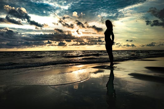 A dramatic silhouette of a woman on the beach at sunset, reflecting on the water.