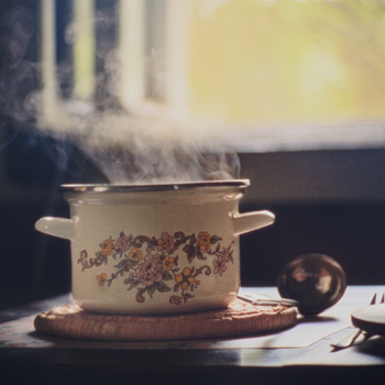 A steaming pot with floral design sits on a rustic table, creating a cozy kitchen ambiance.