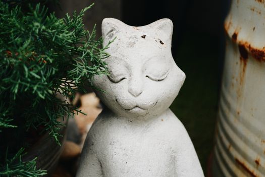 A tranquil cat figurine surrounded by greenery in a rustic garden.