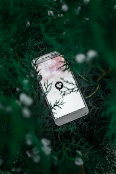 Mobile phone displaying a heart icon nestled among green foliage, creating a tech-nature blend.