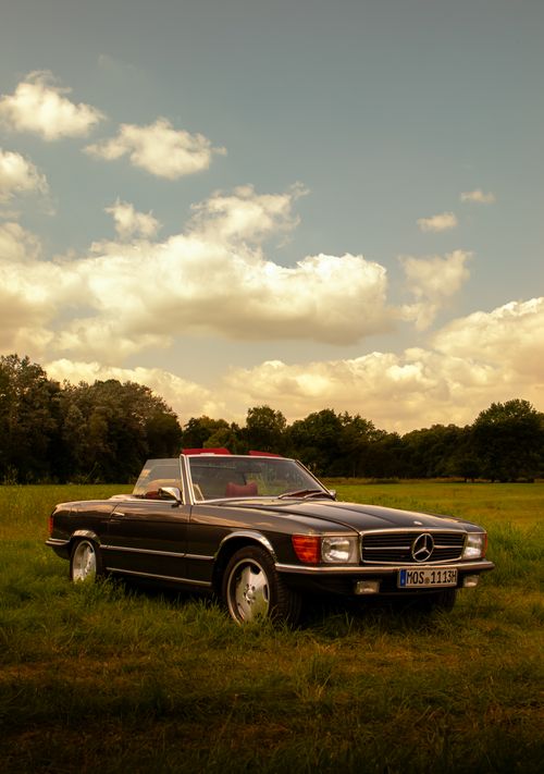 Free Classic Mercedes-Benz convertible parked in a scenic countryside meadow during sunset. Stock Photo