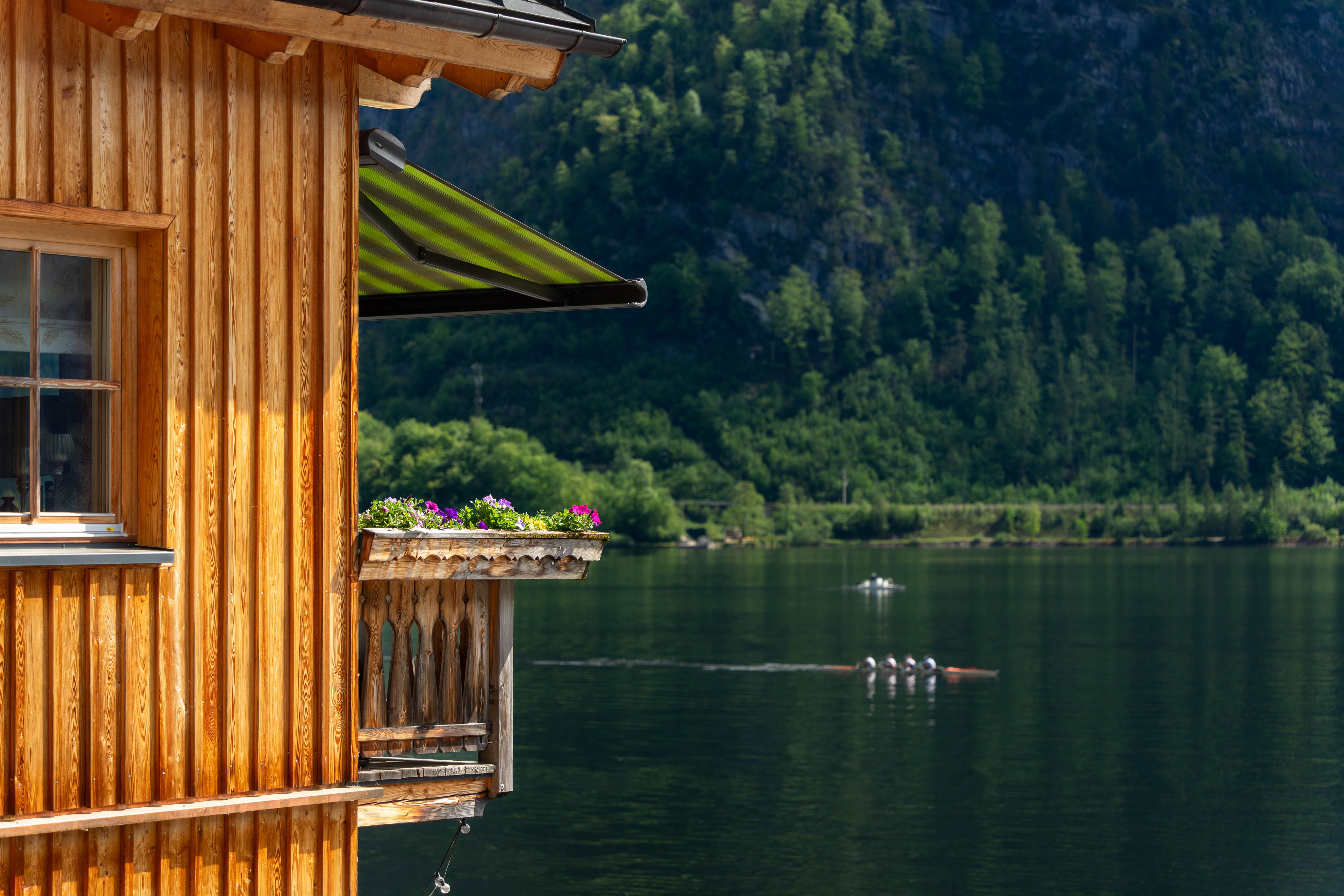 Free Scenic view of a wooden house by the lake in Hallstatt, Austria with lush green hills. Stock Photo