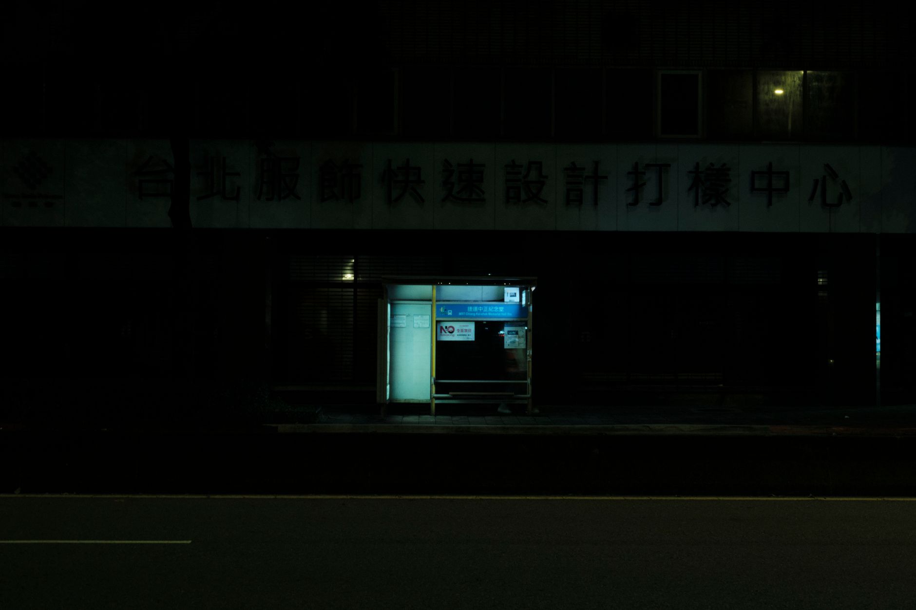 A dimly lit bus stop on a deserted street at night, emphasizing isolation and urban life.