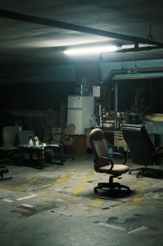 Moody industrial basement scene with scattered office chairs under fluorescent lights, evoking an abandoned workspace feel.