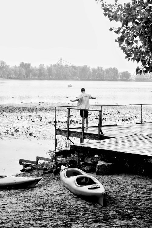Free A man stands on a pier near a river, with canoes and distant trees visible in a serene setting. Stock Photo