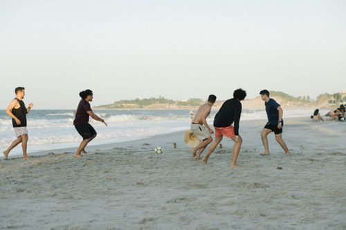 Free A group of young adults enjoying a game of beach soccer by the sea on a sunny day. Stock Photo