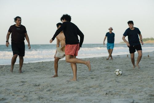 Free Friends enjoying a casual soccer game on a sunny beach, capturing the essence of summer fun. Stock Photo