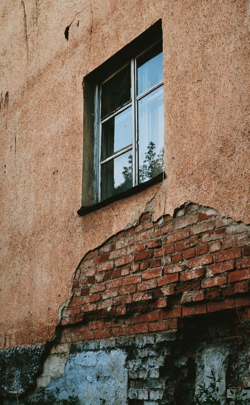 Free A rustic building facade with a cracked brick wall and single window showing signs of age. Stock Photo