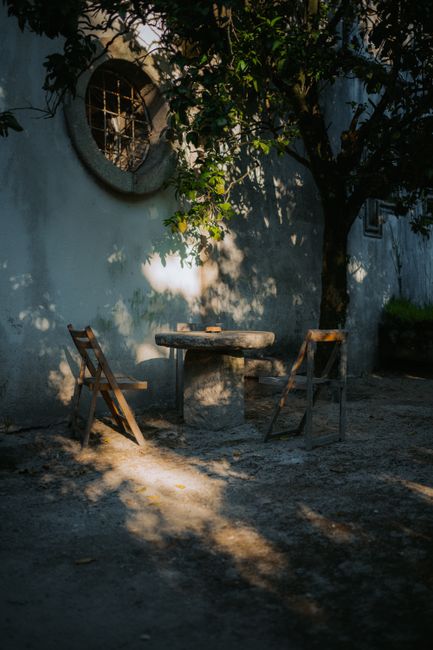 A tranquil outdoor patio with chairs and a rustic table under dappled sunlight.