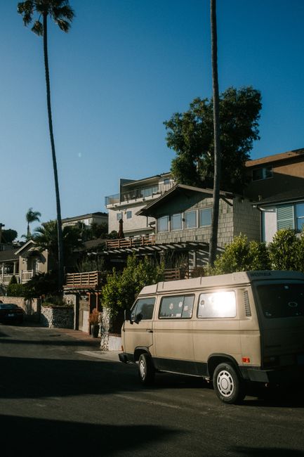 A classic van parked in a picturesque suburban street lined with palm trees and modern homes.