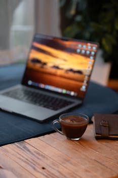 A warm and inviting workspace setup featuring a laptop and a cup of coffee on a wooden table.