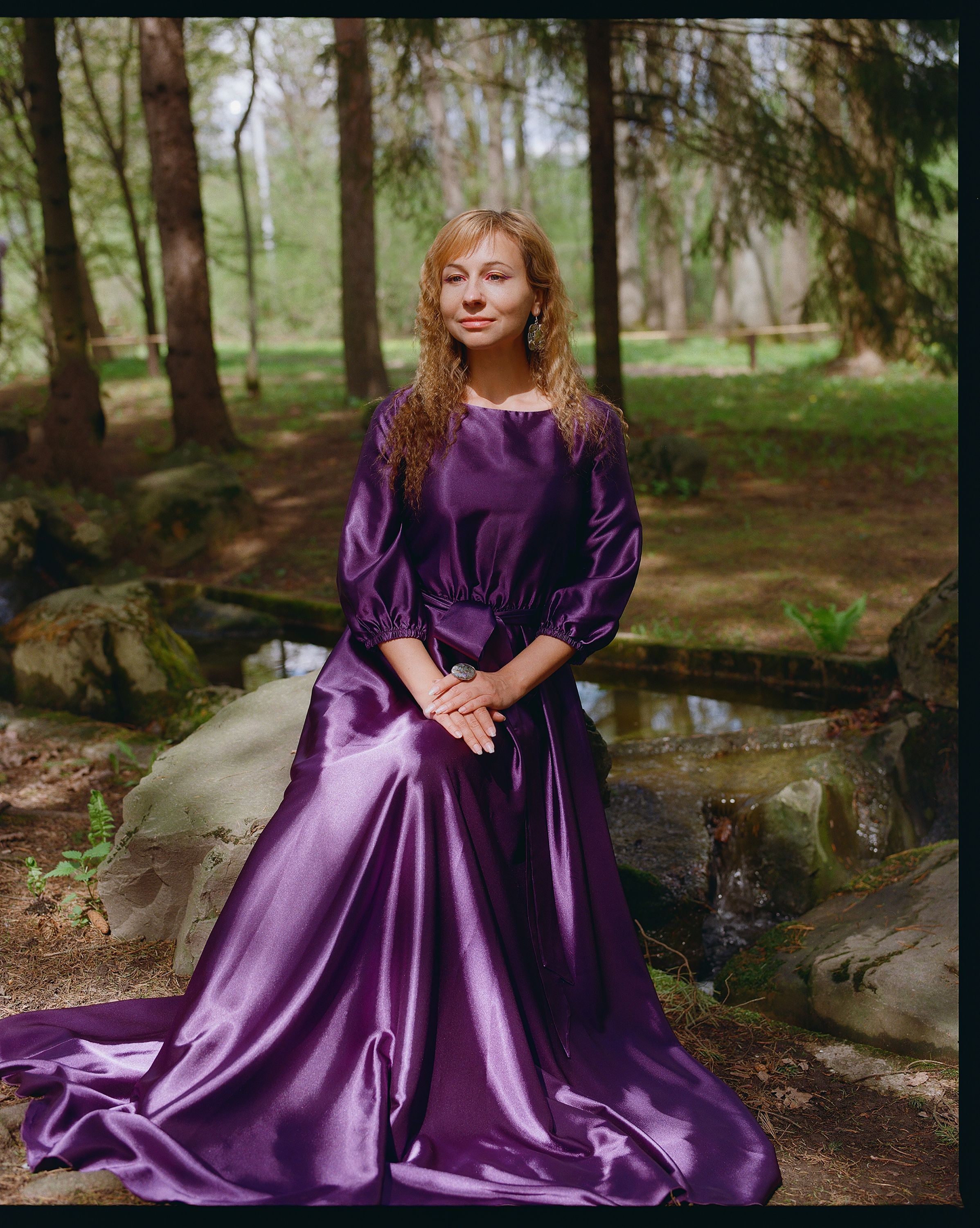 A serene portrait of a woman in a flowing purple gown, surrounded by lush forest greenery.