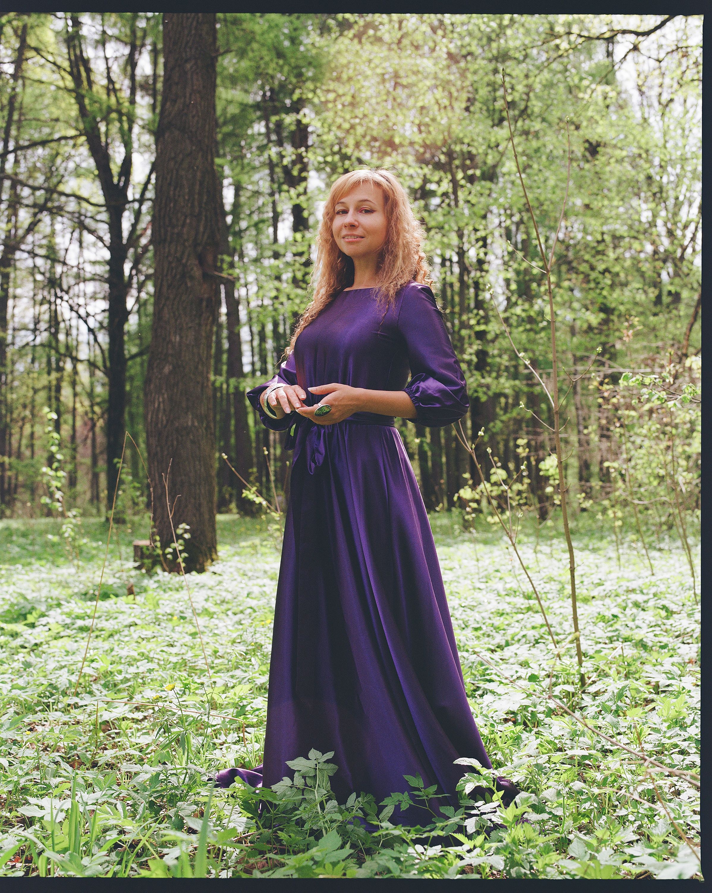 Portrait of a woman in a flowing purple dress surrounded by lush green forest.