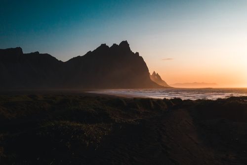 Free Capture of mountainous silhouette at sunset over the calm Icelandic coastline, creating a dramatic and serene scenery. Stock Photo