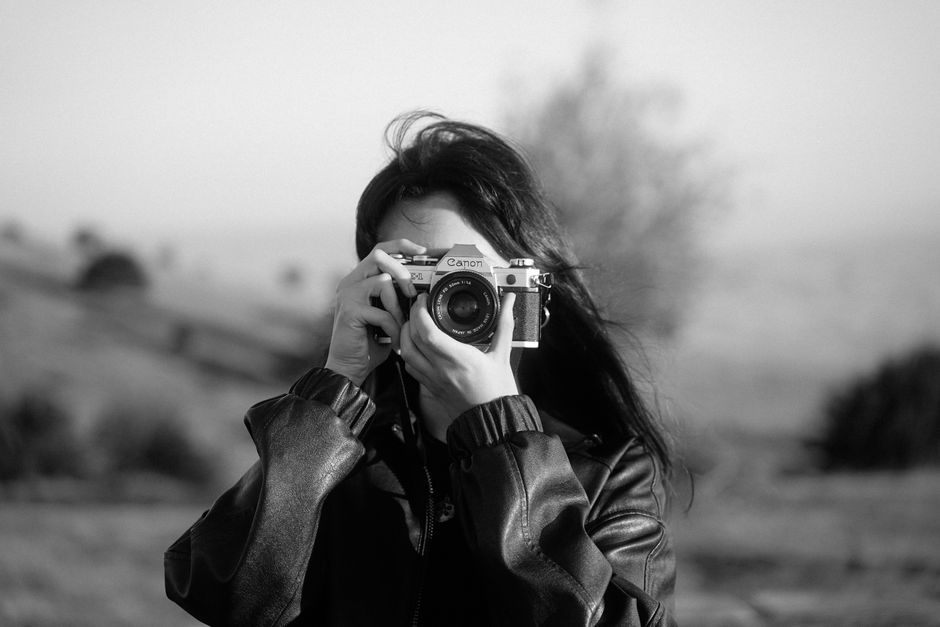 A woman captures a picture outdoors using an analogue camera in a vintage black and white style.