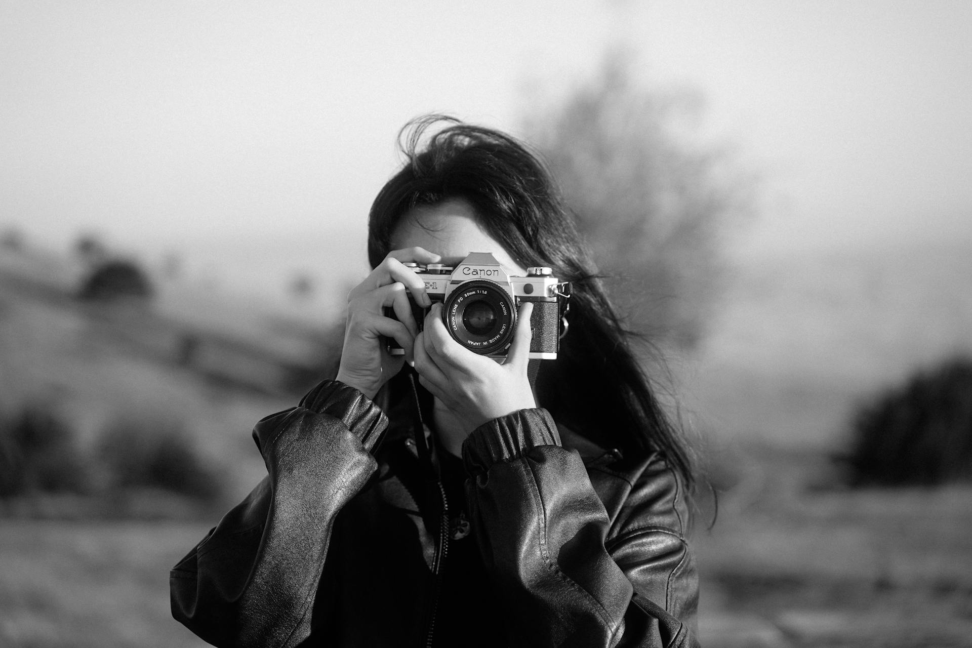 A woman captures a picture outdoors using an analogue camera in a vintage black and white style.