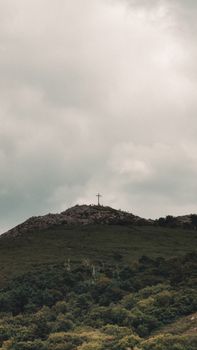 A scenic view of a cross on a grassy hill under a cloudy sky, conveying solitude and peace.