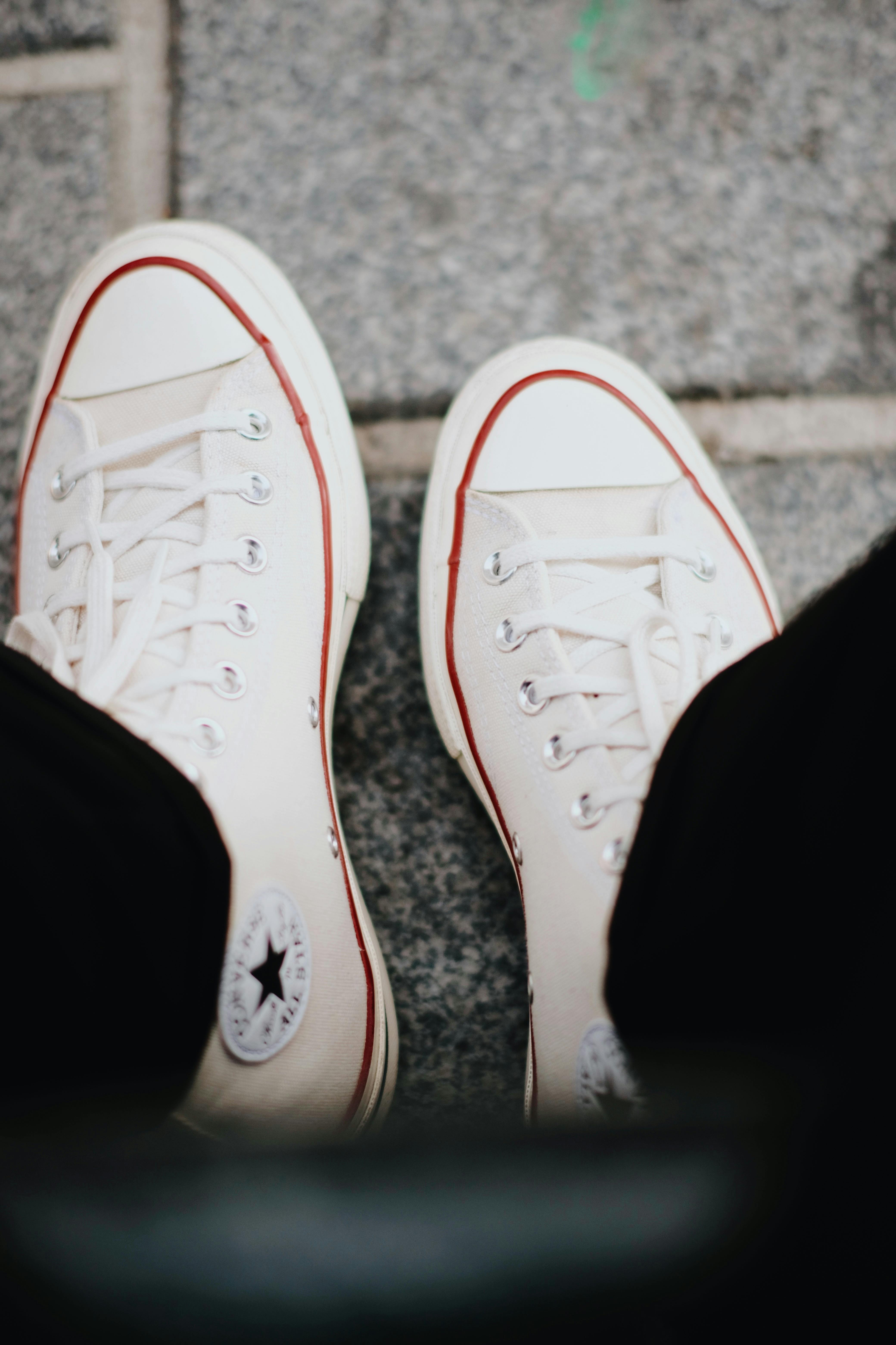 Top view of classic white sneakers with red accents on a city sidewalk.