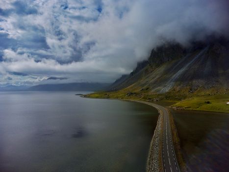 A stunning aerial view of a winding coastal road in Iceland, flanked by serene waters and misty mountains.