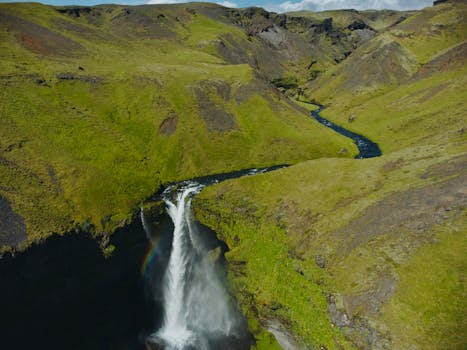 A breathtaking aerial view of a waterfall in Iceland surrounded by lush green hills and valleys.