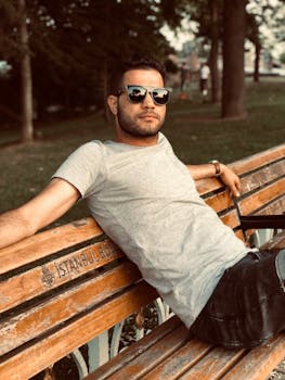 Man in casual wear and sunglasses enjoys a sunny day on a park bench in Istanbul.