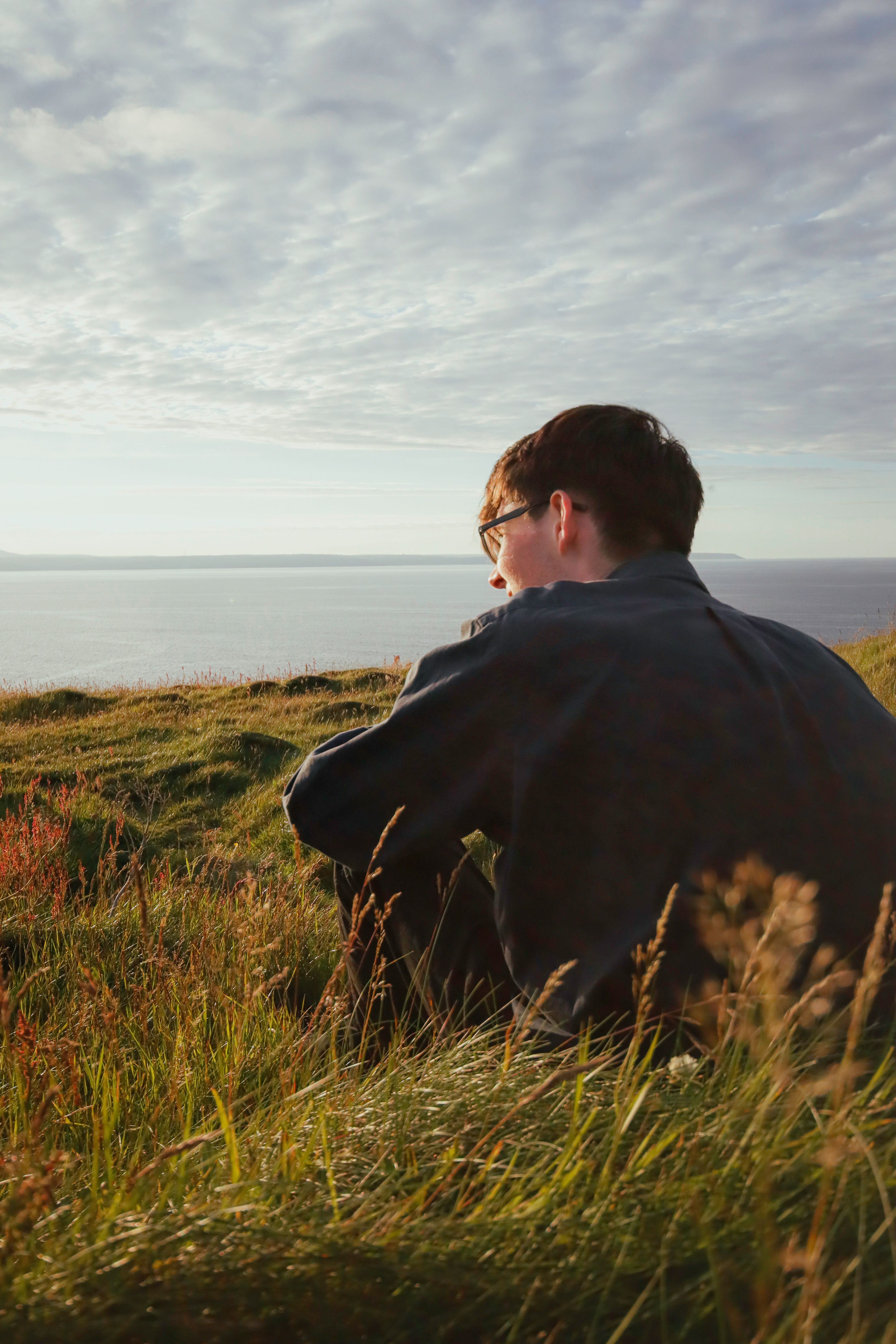 A man sitting on a hill looking out over the ocean · Free Stock Photo