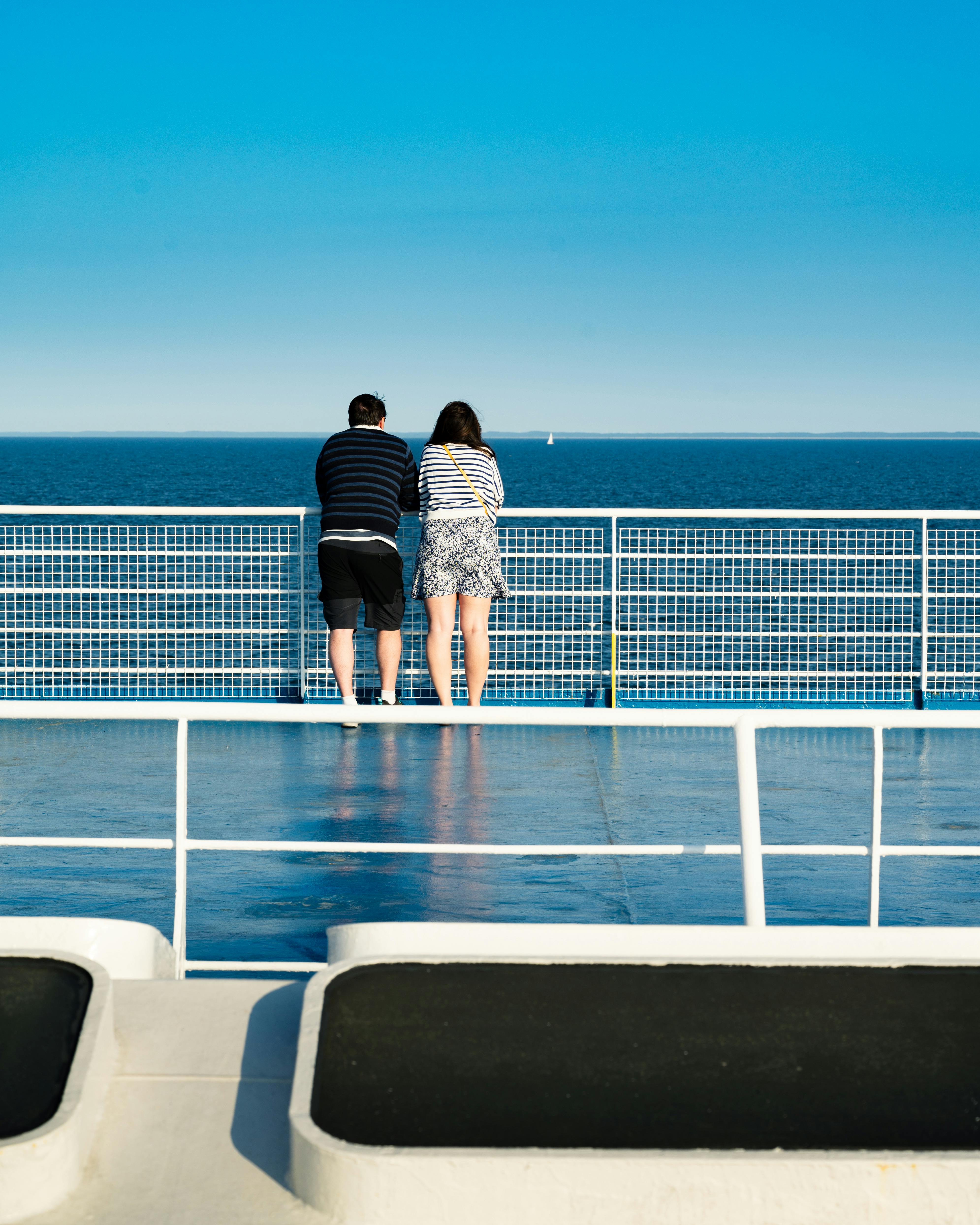 a couple standing on the deck of a ferry looking out at the ocean