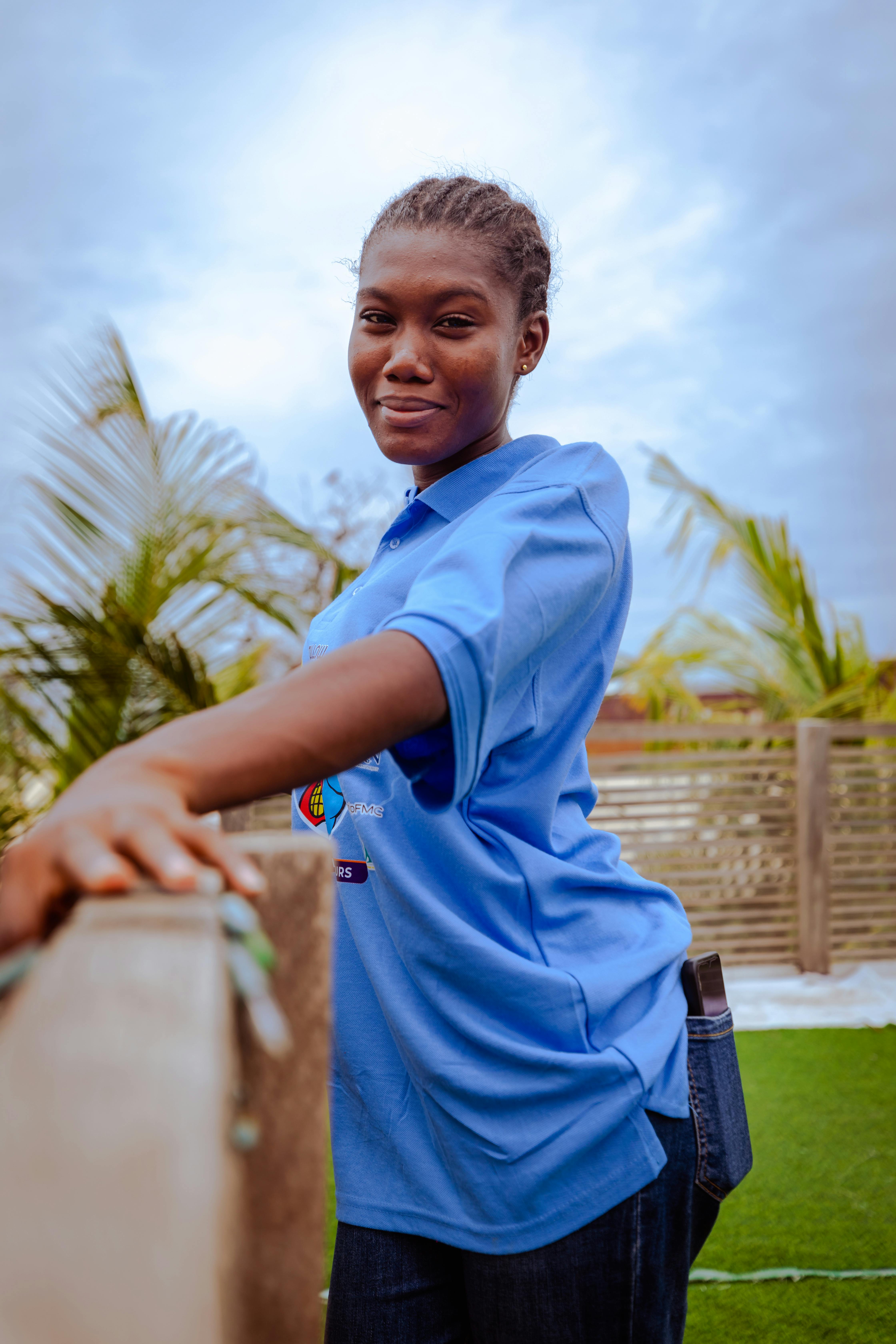 a young woman in a blue shirt leaning on a fence