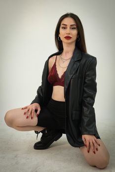 Fashionable woman in leather jacket and red lingerie posing in studio.