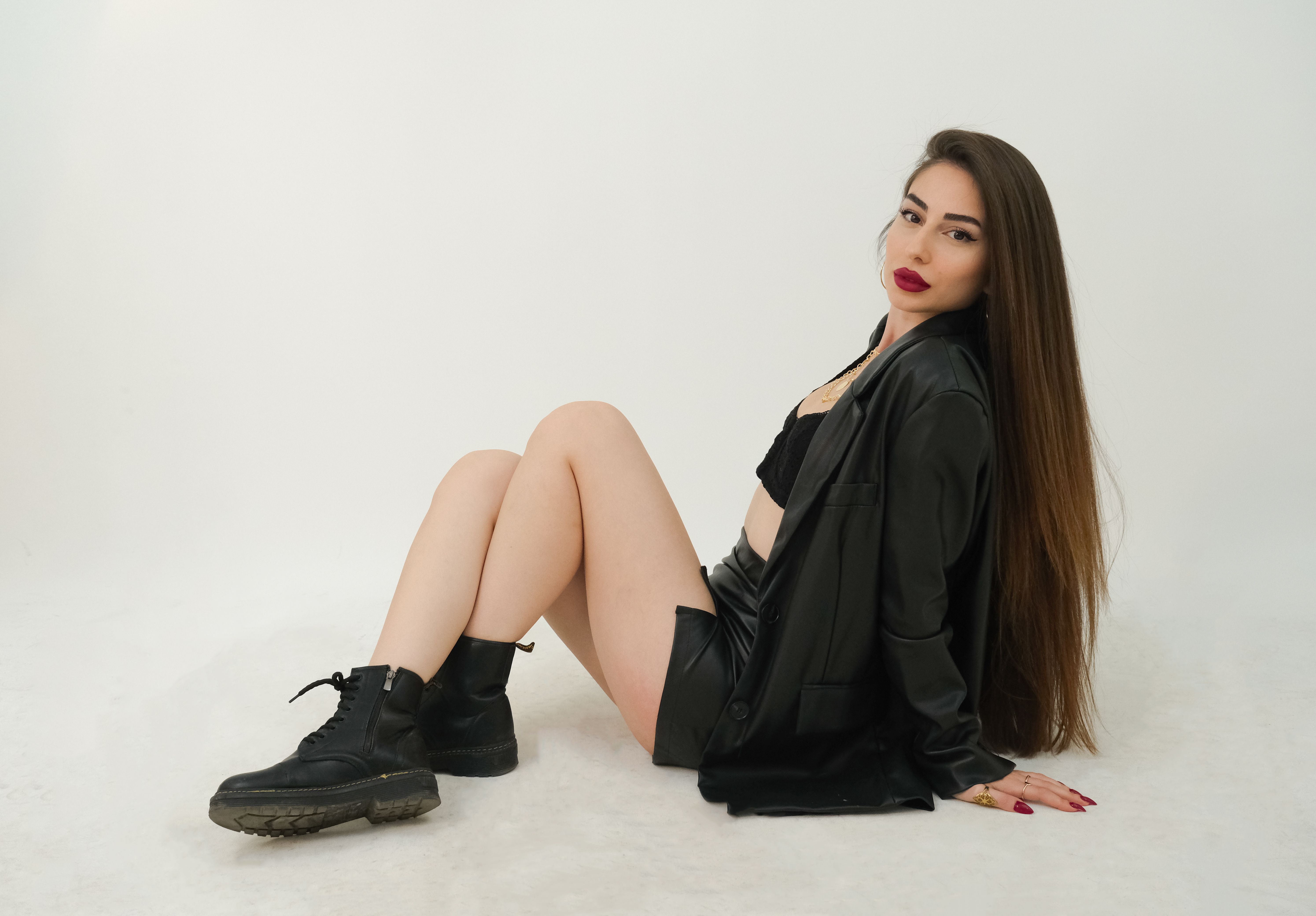 A young woman in a stylish black leather outfit posing elegantly in a studio setting.