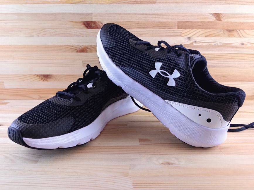Fotomural Elegantes zapatillas deportivas negras exhibidas sobre un suelo de madera, perfectas para deportes y uso casual.