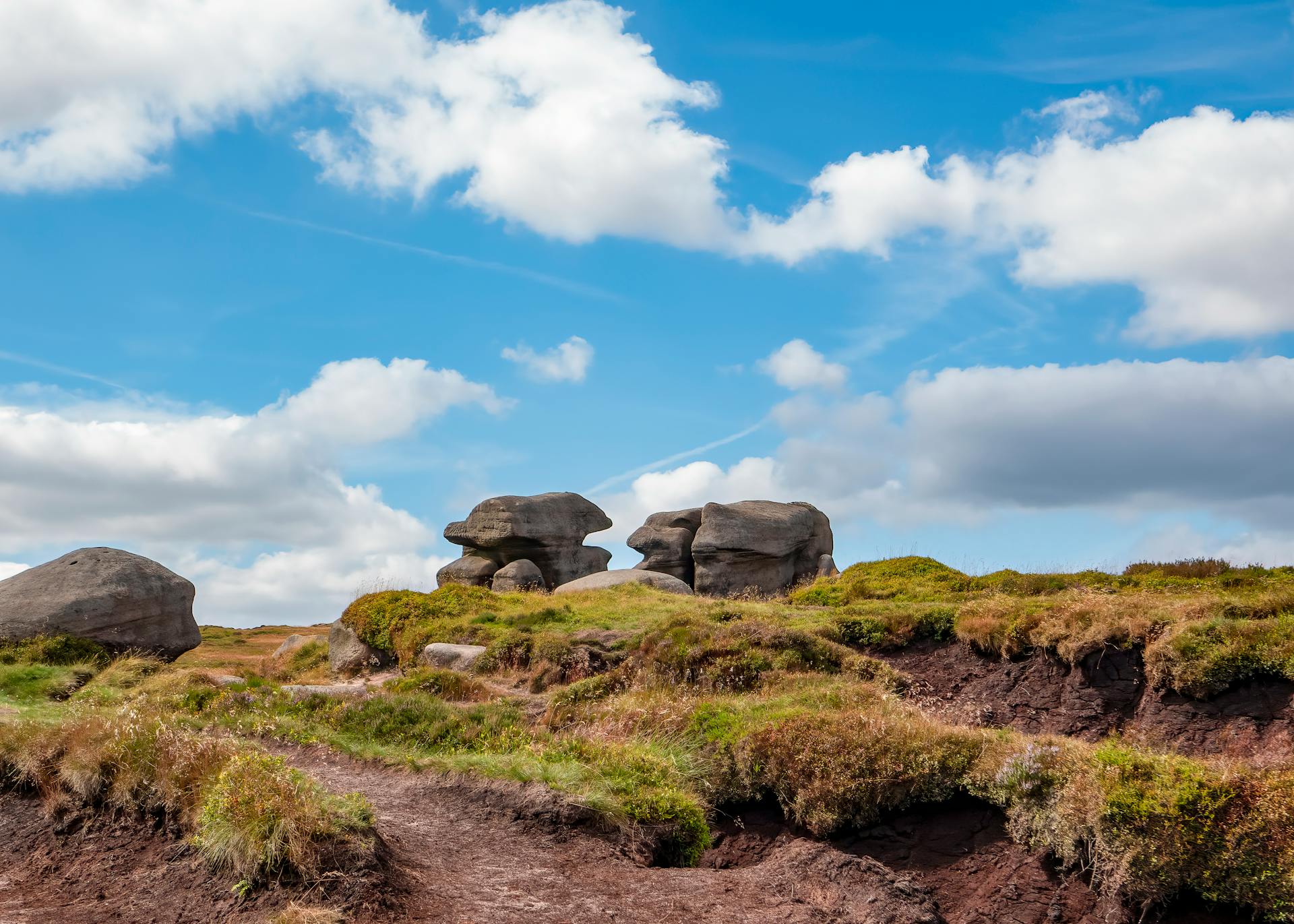 Scenic view of Kinder Scout landscape featuring unique rock formations under a vibrant blue sky.