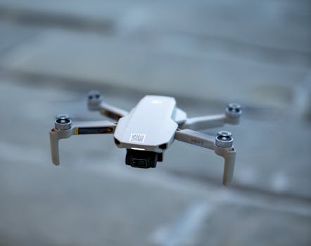 A compact drone in flight against a blurred outdoor backdrop, showcasing advanced technology.
