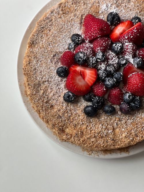 Free Close-up of a homemade cake topped with fresh strawberries and blueberries, dusted with powdered sugar. Stock Photo