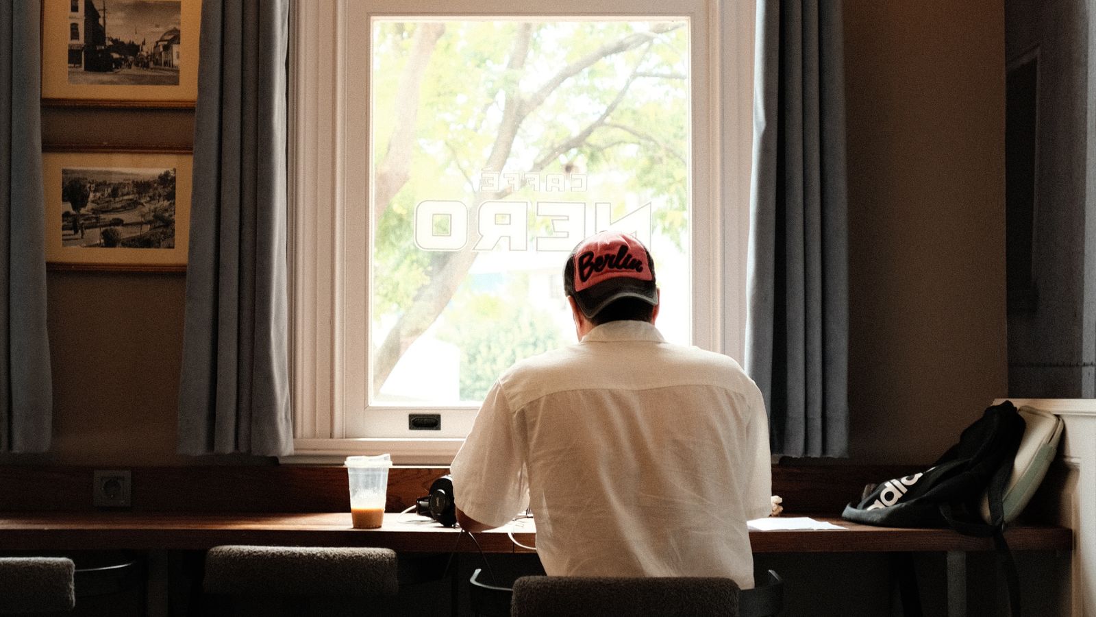 An adult in a cap seated at a counter beside a bright window